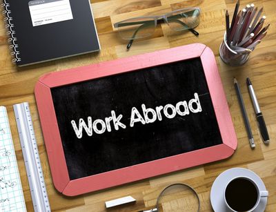 Auf einem Schreibtisch liegt neben Stiften und anderen Dingen eine Tafel mit den Worten "Work Abroad".