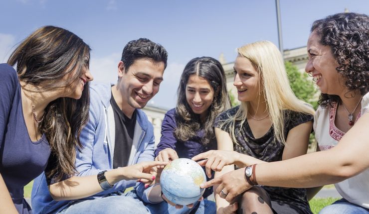 Das Bild zeigt International Studierende mit einem Globus in der Hand. 