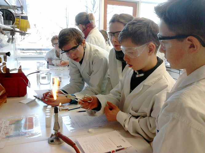 Children in white coats and protective masks stand at the Bunsen burner in the laboratory