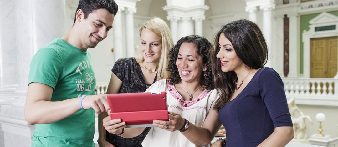 Foto: vier Studierende stehen zusammen und blicken auf ein Tablet