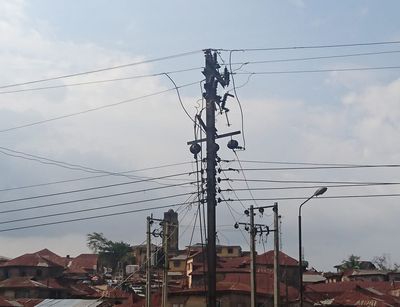Ein Elektrizitätsmast und von ihm ausgehende Kabel von unten fotografiert vor dem Hintergrund eines Stadtteils von Ibadan, Nigeria.