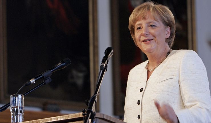 Foto: Dr. Angela Merkel steht am Rednerpult, in einem weißem Jacket gekleidet mit freudigem Gesichtsausdruck