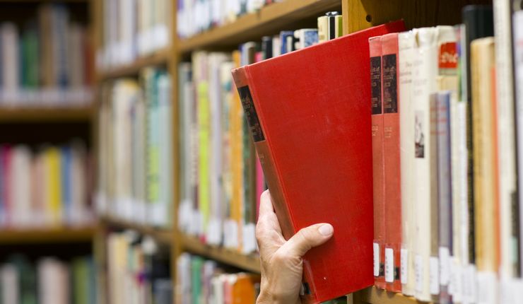 Eine Hand greift ein Buch aus einem Bibliotheksregal, Foto: Colourbox