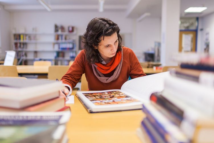 Student sits at a table in the art library and looks into a book