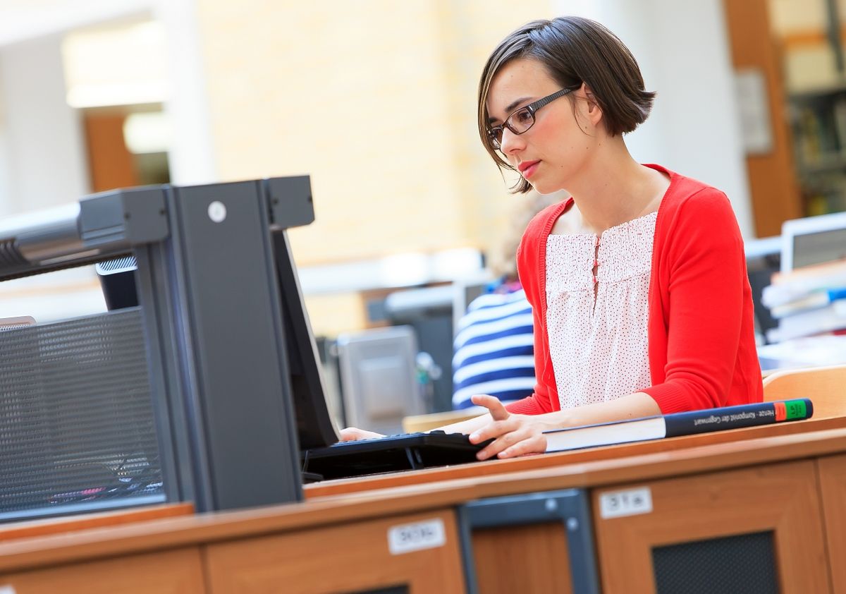 zur Vergrößerungsansicht des Bildes: Foto: Eine Junge Frau sitzt in der Universitätsbibliothek am Laptop