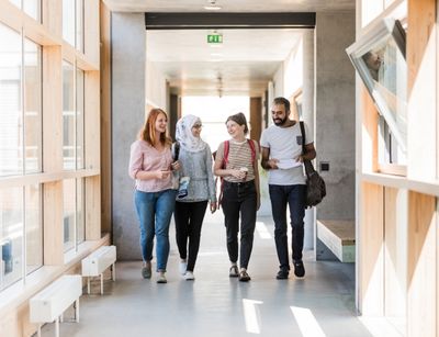 Studierende der Universität Leipzig laufen durch einen Gang des Geisteswissenschaftlichen Zentrums. Das Gebäude ist hell, die Studierenden wirken fröhlich.