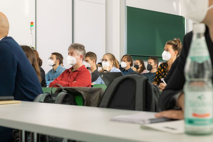 People wearing respiratory masks in a lecture hall sitting and listening to a talk