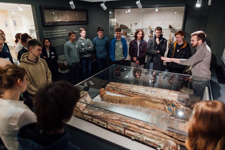 Das Foto zeigt eine Gruppe junger Menschen, die um ein Ausstellungsobjekt stehen. 