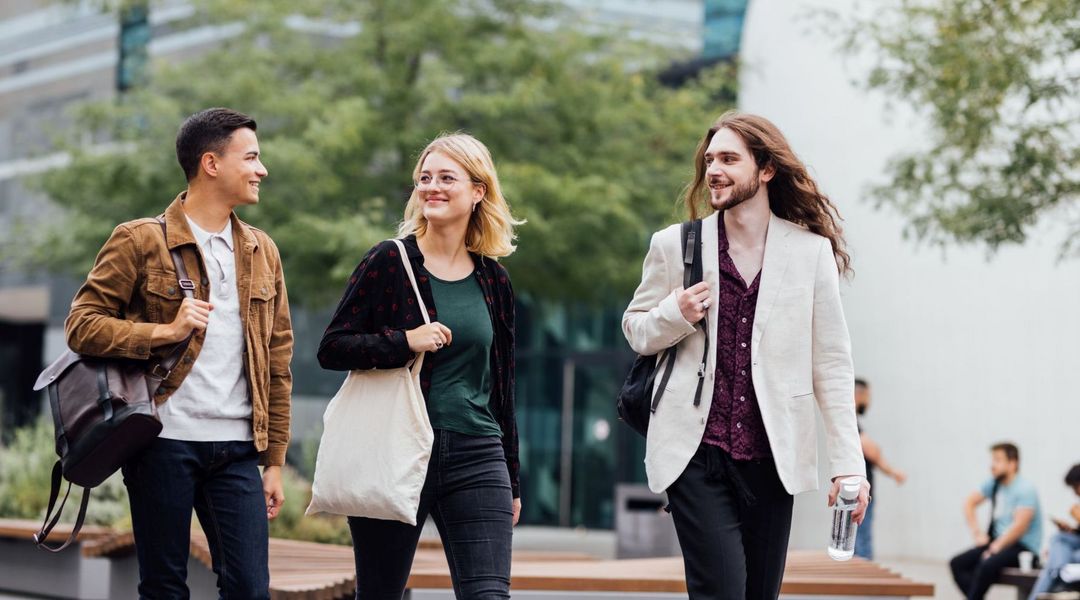 Drei Studierende laufen über den Campus Augustusplatz und reden miteinander, Foto: Christian Hüller