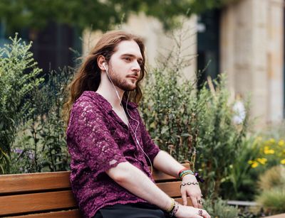 Student mit langen Haaren sitzt auf der Bank auf dem Campus mit Kopfhörern, Foto: Christian Hüller