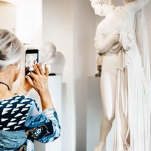 Besucherin hält ein Handy hoch und fotografiert eine Statue.
