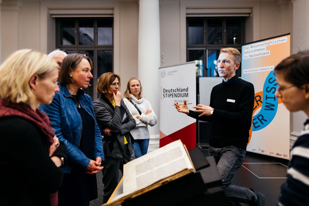 zur Vergrößerungsansicht des Bildes: Dr. Christoph Markert steht vor eine Gruppe von Gästen und erläutert die mittelalterlichen Handschriften, die er erforscht