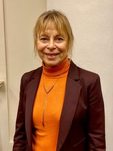 Porträtfoto von Frau Dr. Petra Tschoppe, sie trägt einen orangefarbenen Rollkragenpullover, ein schokobraunes Sakko und eine silberfarbene Kette