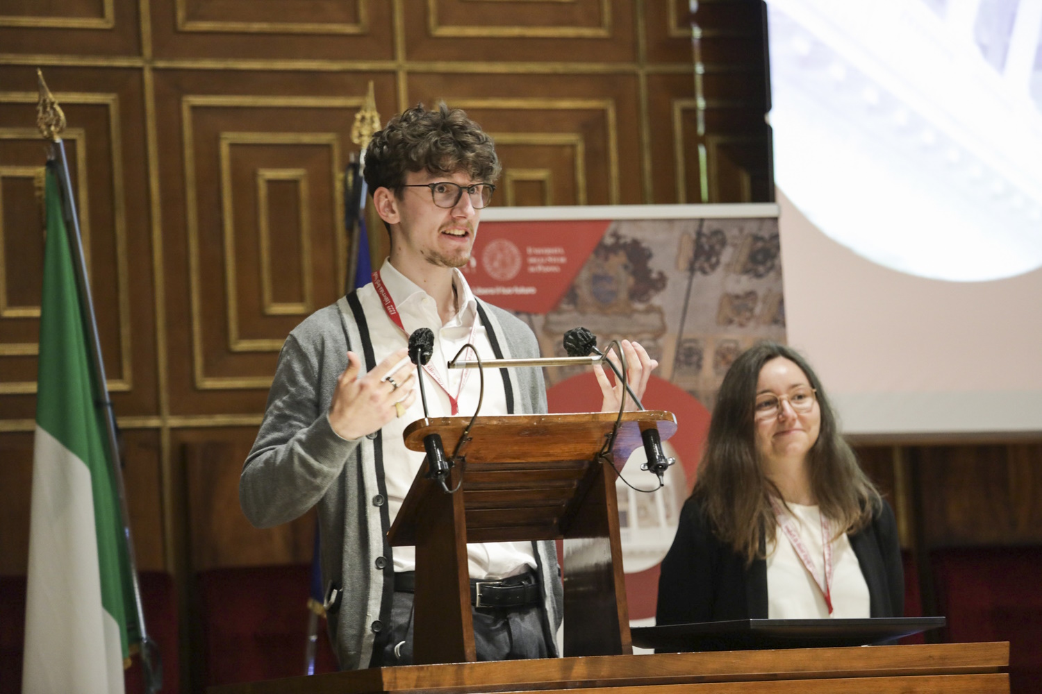 zur Vergrößerungsansicht des Bildes: Studierendenvertreter Benedikt Grothe hält eine Rede bei der Arqus Jahrsversammlung hinter einem PUlt stehend