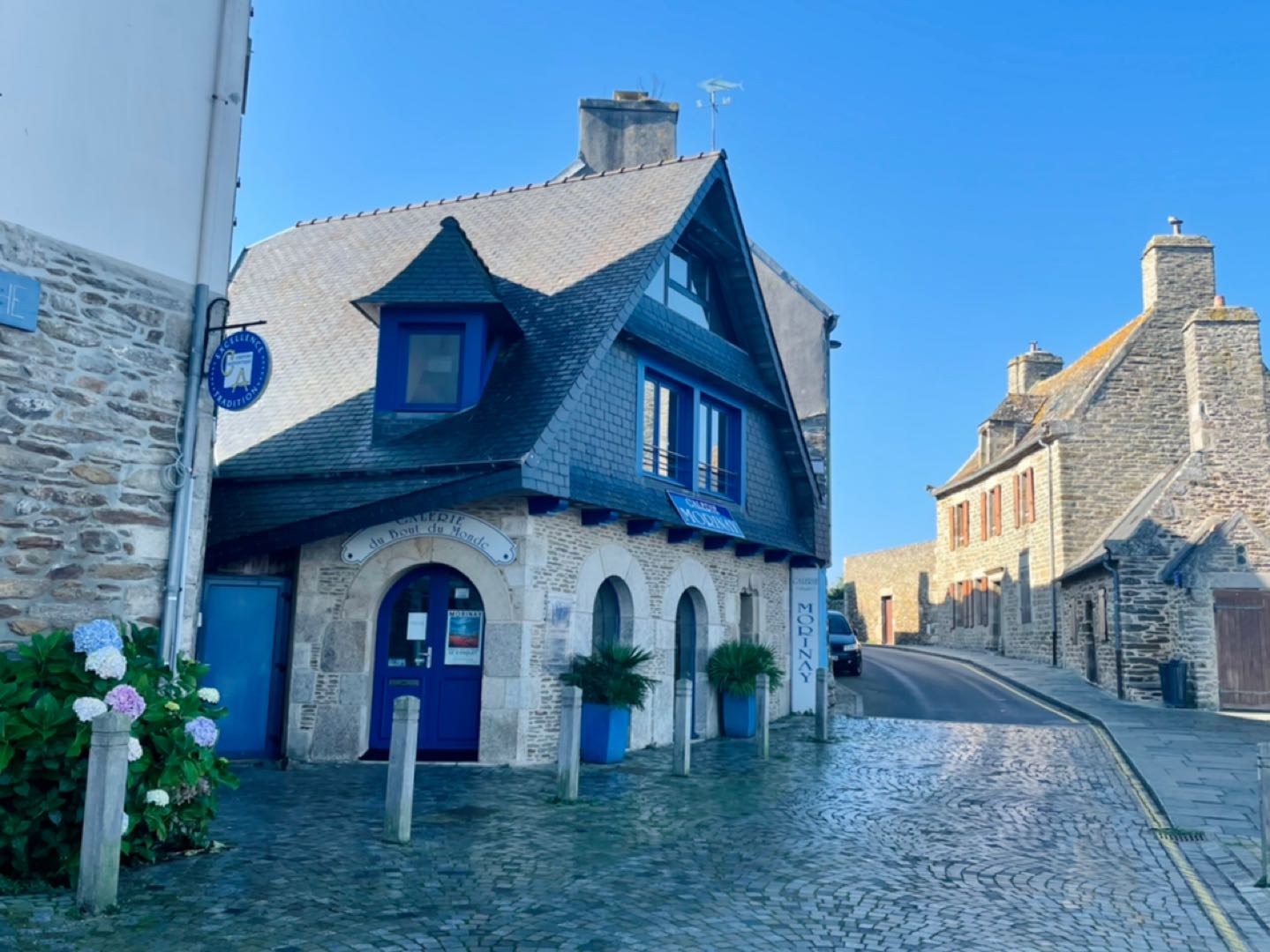 Zu sehen ist die pittoreske Stadt Le Conquet. Kleine Steinhäuser säumen eine sich hinauf windende Straße aus Kopfsteinpflaster.