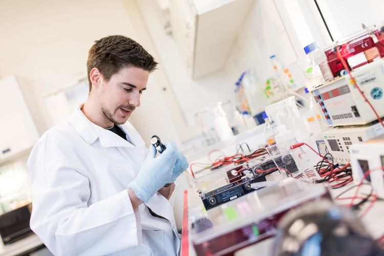 Zu sehen ist ein Mann in einem Labor, beim Experimentieren an einem Labortisch, der voller Instrumente ist.