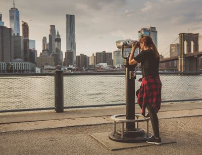 Frau schaut durch ein Fernrohr auf eine Stadt mit Wolkenkratzern