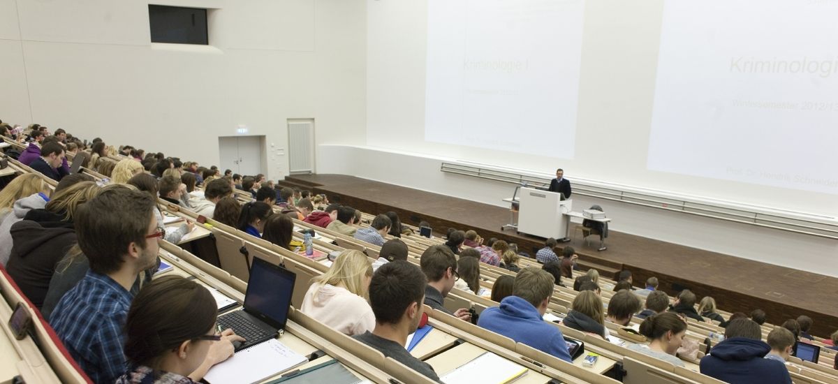 Foto: Vorlesung im vollbesetzten Audimax, am Rednerpult steht ein Professor