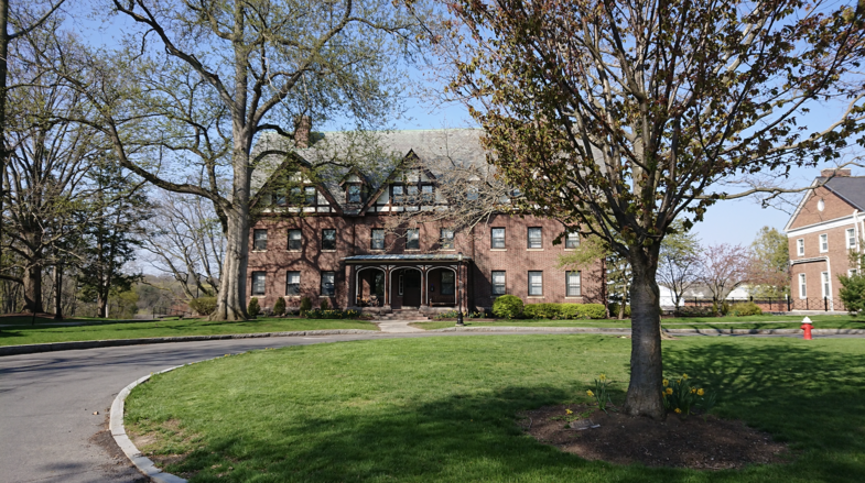 Ein typisch US-amerikanisches Haus steht im Bildhintergrund. Davor sind Bäume und Rasen zu sehen.