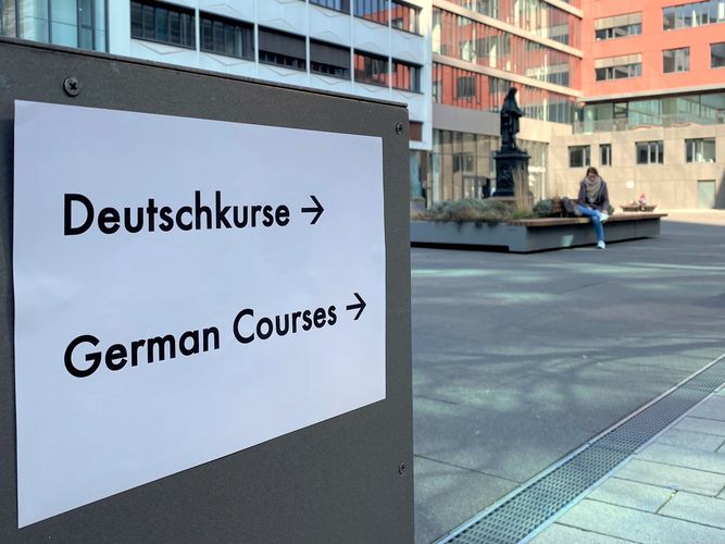 Schild hängt an der Tür zum Hörsaalgebäude mit der Aufschrift "Deutsch-Kurse" auf Deutsch und Englisch.