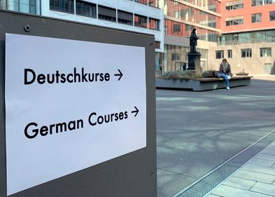 Schild hängt an der Tür zum Hörsaalgebäude mit der Aufschrift "Deutsch-Kurse" auf Deutsch und Englisch.