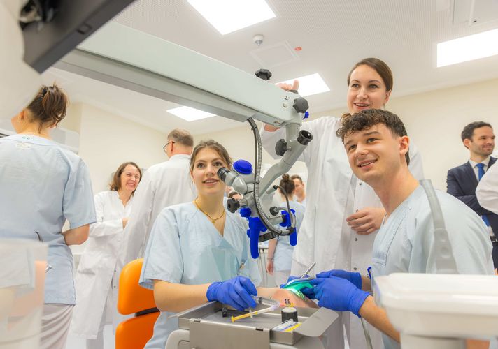 Zu sehen sind Studierende, die an einer Puppe, die auf einem Behandlungsstuhl liegt, eine Zahnbehandlung üben.