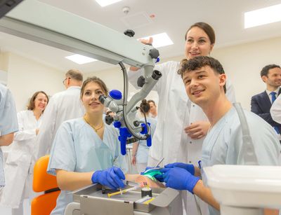 Zu sehen sind Studierende, die an einer Puppe, die auf einem Behandlungsstuhl liegt, eine Zahnbehandlung üben.