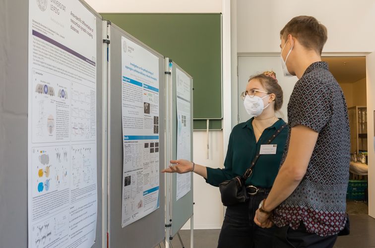 A man and a woman with respiratory masks standing and discussing in front of the poster