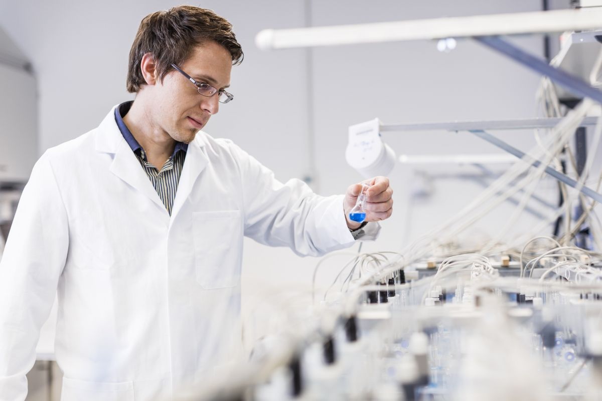 zur Vergrößerungsansicht des Bildes: Professor Nico Eisenhauer steht im Labot und betrachtet ein Reagenzglas, in dem eine blaue Flüssigkeit ist.