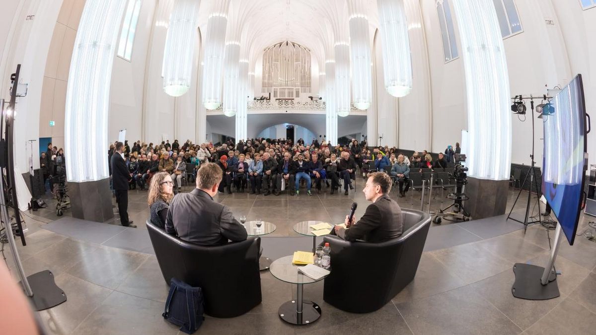 zur Vergrößerungsansicht des Bildes: Prof. Dr. Maren Möhring und Prof. Dr. Matthias Blüher sitzen mit dem Rücken zur Kamera auf dem Podium im Paulinum und berichten dem Publikum über ber ihren Exzellenz-Antrag "Adipositas verstehen".