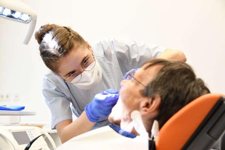 Studentin mit Mundschutz behandelt Patienten in der Zahnklinik, Foto: Anton Stolle