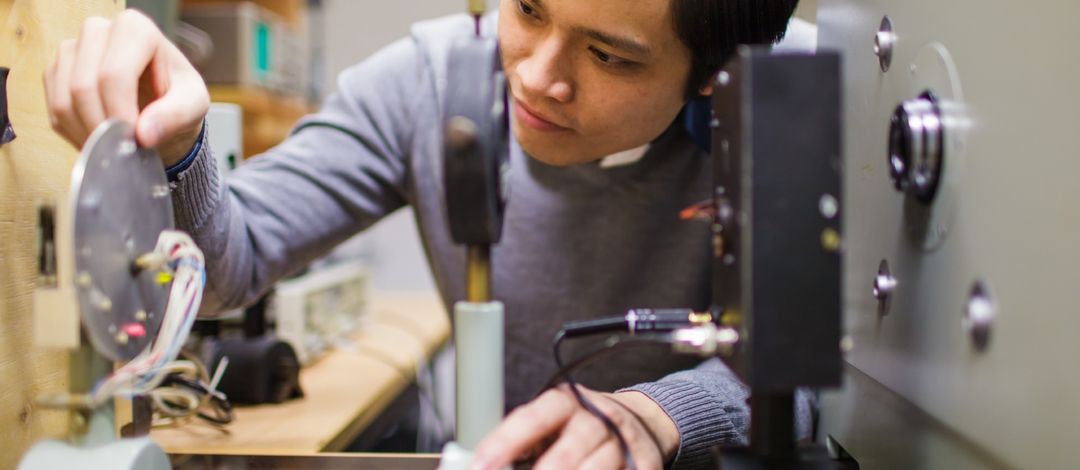 Foto: ein junger Mann, asiatischer Herkunft, experimentiert im Physiklabor