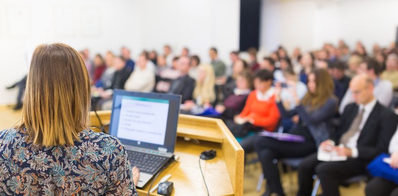 Zu sehen ist eine Frau, die auf einer Konferenz einen Vortrag hält.