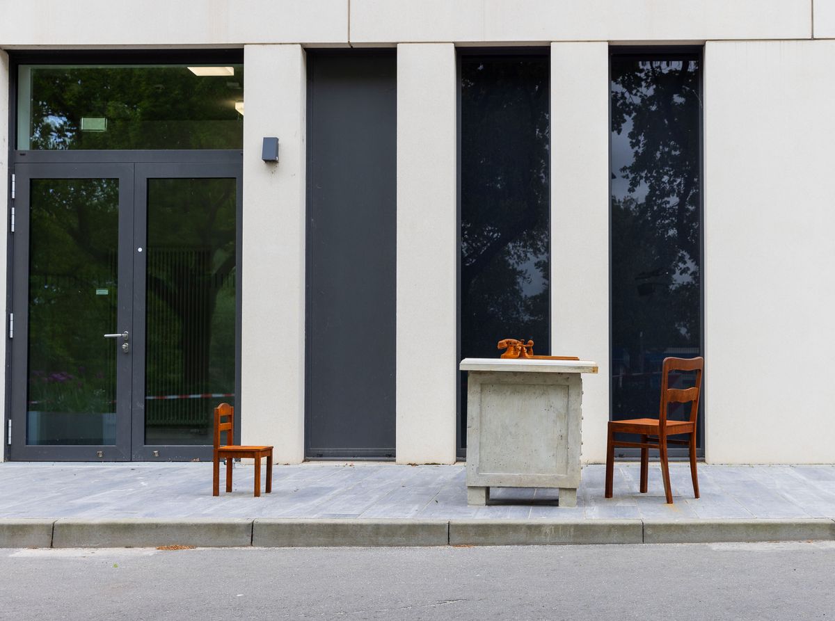 zur Vergrößerungsansicht des Bildes: Ansicht des Mahnmals "Schreibtisch". Vor einem in Beton gegossenen Schreibtisch mit Stuhl steht ein kleiner Kinderstuhl.