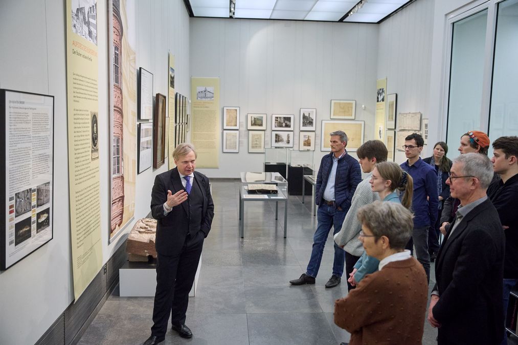 zur Vergrößerungsansicht des Bildes: Förderer und Stipendiaten stehen in der Galerie im neuen Augusteum, auf der linken Seite steht der Kustos und spricht zu den Gästen, die auf der rechten Seite zu sehen sind
