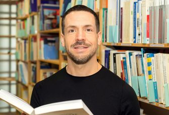 Prof. Klaus Grübel steht mit einem offenen Buch in der Bibliothek