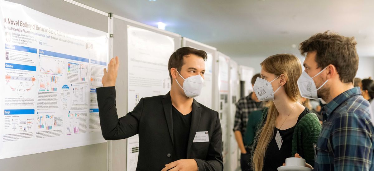 Two man and a woman with respirator face masks standing in front of a poster wall