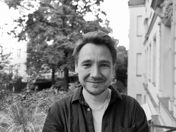 Schwarz-Weiß-Foto von Christian Rau, im Hintergrund ein Teil eines Wohnhauses und ein Hinterhof