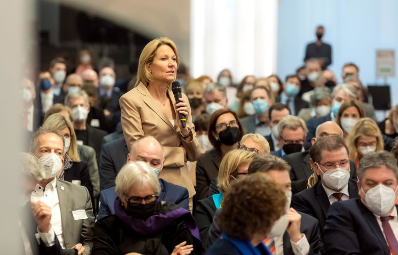 Eine Frau steht im Publikum und stellt mit Mikro in der Hand eine Frage