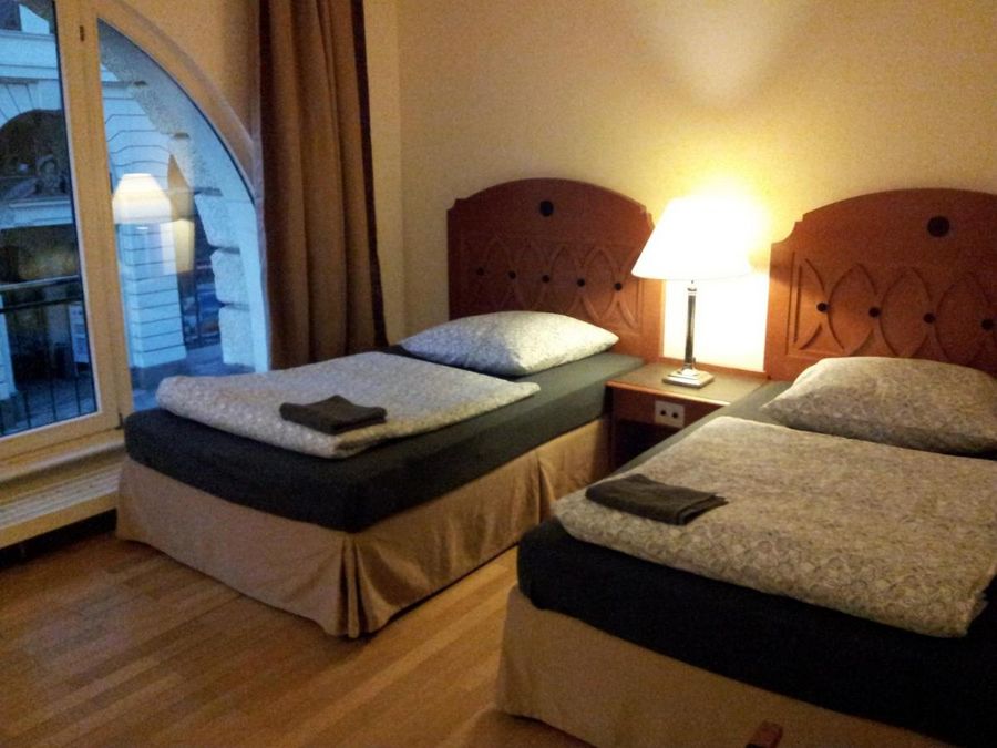 enlarge the image: Farbfoto: Innaufnahme eines Wohnraums mit zwei Betten, einem Nachttischt, einer Stehlampe und bodentiefen Fenstern