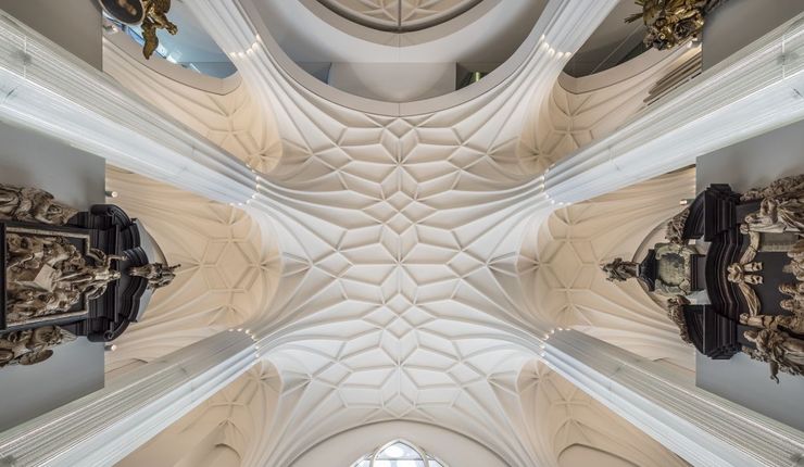Architekturfoto: Blick von unten nach oben auf das Gewölbe im Paulinum, welches mit seinen Säulen und der Struktur an der Decke an eine Kirche erinnert.