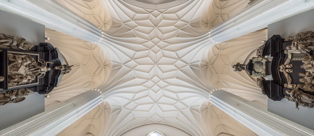 Architekturfoto: Blick von unten nach oben auf das Gewölbe im Paulinum, welches mit seinen Säulen und der Struktur an der Decke an eine Kirche erinnert.