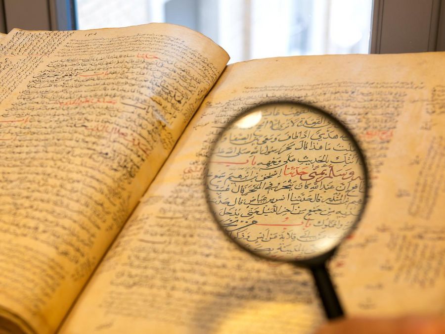 zur Vergrößerungsansicht des Bildes: Eine Lupe wird auf ein arabisches Buch gehalten