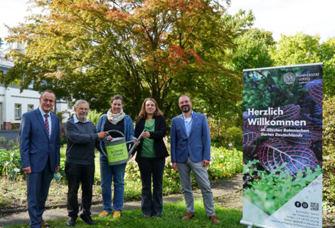 Menschen stehen nebeneinander im Botanischen Garten mit einer Gießkannie in der Hand