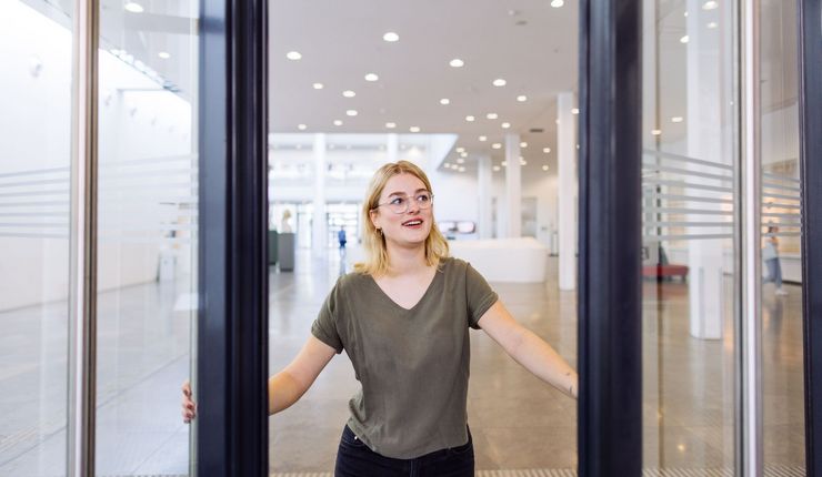 Studentin öffnet mit einem Lächeln die Tür zum Neuen Augusteum, Foto: Christian Hüller