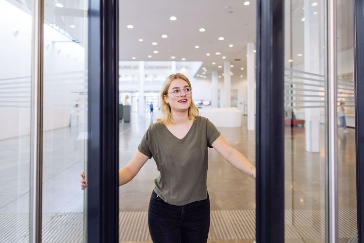 Studentin öffnet mit einem Lächeln die Tür zum Neuen Augusteum, Foto: Christian Hüller