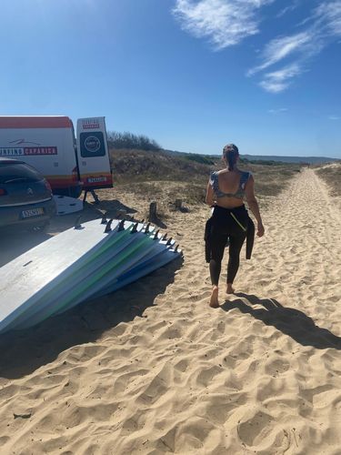 Surfschule am Rande einer Düne, eine Person mittig im Bild mit Neoprenanzug, im HintergrundKüste und blauer Himmel