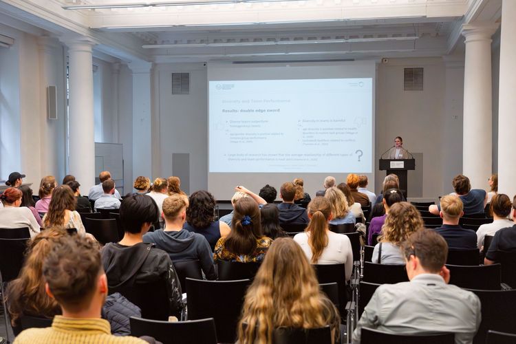 In einem Seminarraum sitzen viele Zuhörer:innen und hören einer Referentin zu