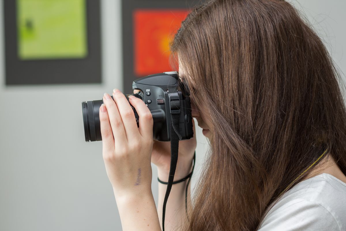 zur Vergrößerungsansicht des Bildes: Zu sehen ist eine Jugendliche mit einer Kamera. Sie stellt den Fokus ein.