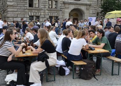 Junge Menschen sitzen auf Bierbänken und an Biertischen auf dem Leipziger Burgplatz. 